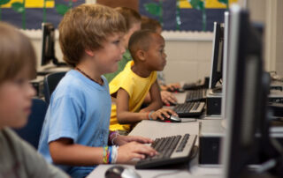 A group of young students learning in a classroom with a computer and keyboard