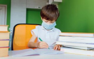 ired boy studying at home in a protective face mask during CoVid-19 quarantine, distance learning online with a laptop, a child doing homework for school. Schoolboy stayed at home.