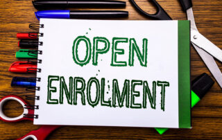 age of the words, Open Enrollment, written on a notebook on top of pens, markers, scissors, highlighter on a wooden background