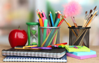 School supplies, such as, colored pencils, markers, paint brushes, notebooks, Post-It notes, red apple on a wooden desk