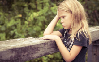 Image of a sad young blonde girl standing on a wooden bridge deep in thought during the day